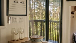 A wooden table with a bowl and glasses, a 'WELCOME' sign, and a view of a deck with trees. - Sowilo Pine House. All-inclusive food and drinks. (Cambridge)