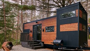 A modern cabin with a wooden exterior and black accents, featuring a deck, outdoor seating, and a grill area. - Sowilo Pine House. All-inclusive food and drinks. (Cambridge)