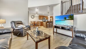 A modern living room with leather sofas, a coffee table, and a TV displaying a beach scene. - Sunset Splash Cabin at Bridges Bay Resort (Arnolds Park)