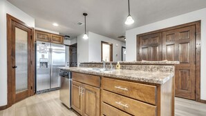 A modern kitchen with wooden cabinets, a granite countertop, stainless steel appliances, and pendant lighting. - Sunset Splash Cabin at Bridges Bay Resort (Arnolds Park)