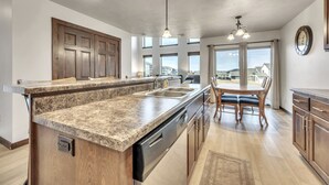 A modern kitchen with granite countertops, a built-in dishwasher, wooden cabinets, and pendant lighting. - Sunset Splash Cabin at Bridges Bay Resort (Arnolds Park)