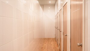 A hallway with tiled walls and wooden flooring, leading to a row of wooden doors. - The Dorm Hostel (Phuket)