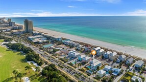 An aerial view of a coastal town with a beachfront, residential buildings, and a large hotel with a swimming pool. - Large Panama City Beach Home |Heated Private Pool | Easy Beach Days (Panama City Beach)