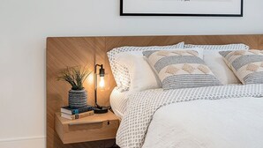 A neatly arranged bedroom with a wooden headboard, a bedside table with a lamp, and a framed artwork on the wall. - West Bay Bliss (Victoria)