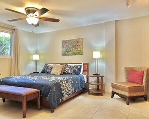A bedroom with a bed, two bedside lamps, a ceiling fan, a bench, a chair, and a painting on the wall. - OASIS Apartments Simpson Bay (Simpson Bay)