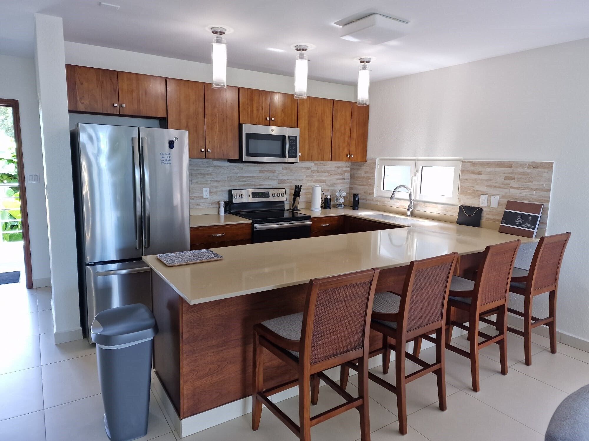 A modern kitchen with wooden cabinets, stainless steel appliances, a large island with bar stools, and a trash bin.