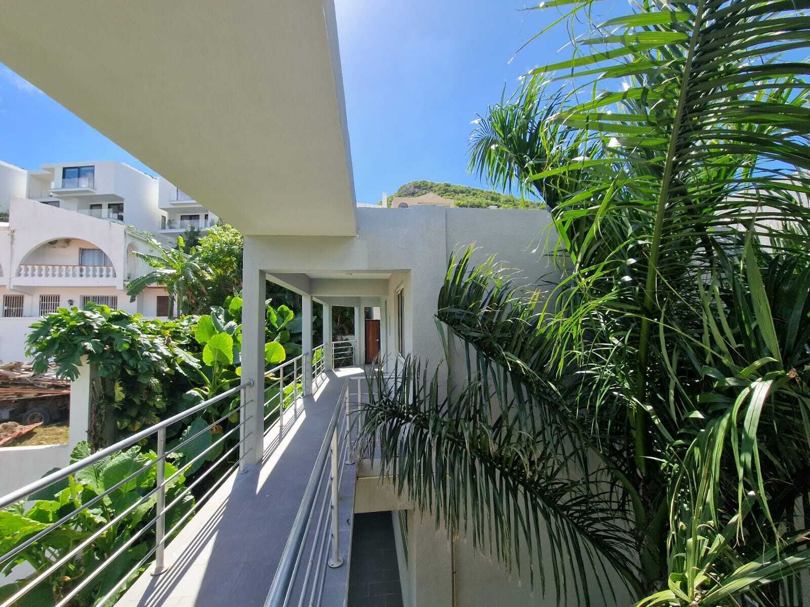 A modern building with a covered outdoor area, featuring a metal railing and lush greenery.
