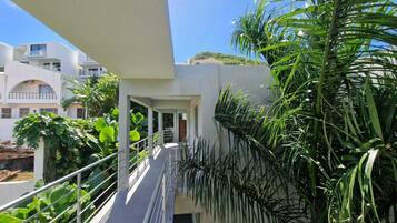 A modern building with a covered outdoor area, featuring a metal railing and lush greenery.