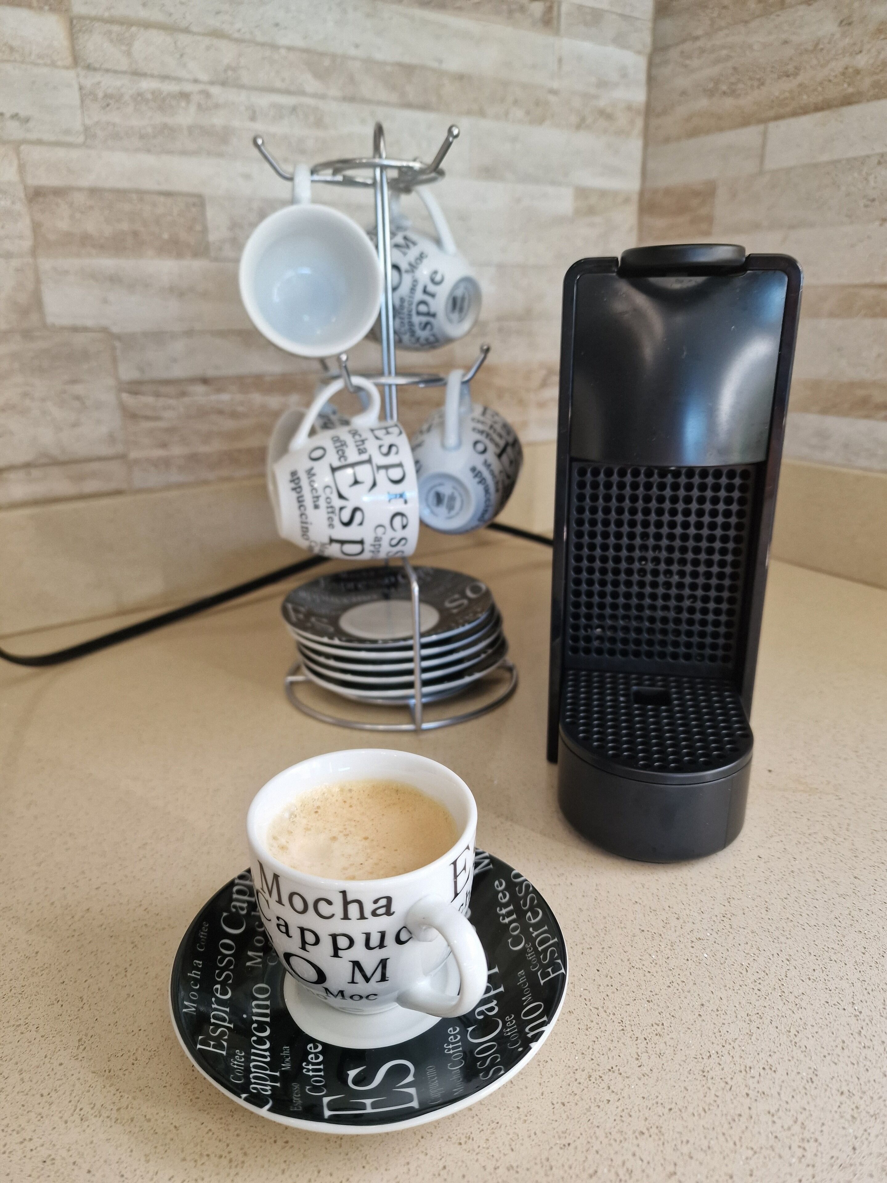 Eine Kaffeestation mit einer Tasse Kaffee auf einem Untertasse, einer Kaffeemaschine und einem Becherständer mit mehreren Tassen.