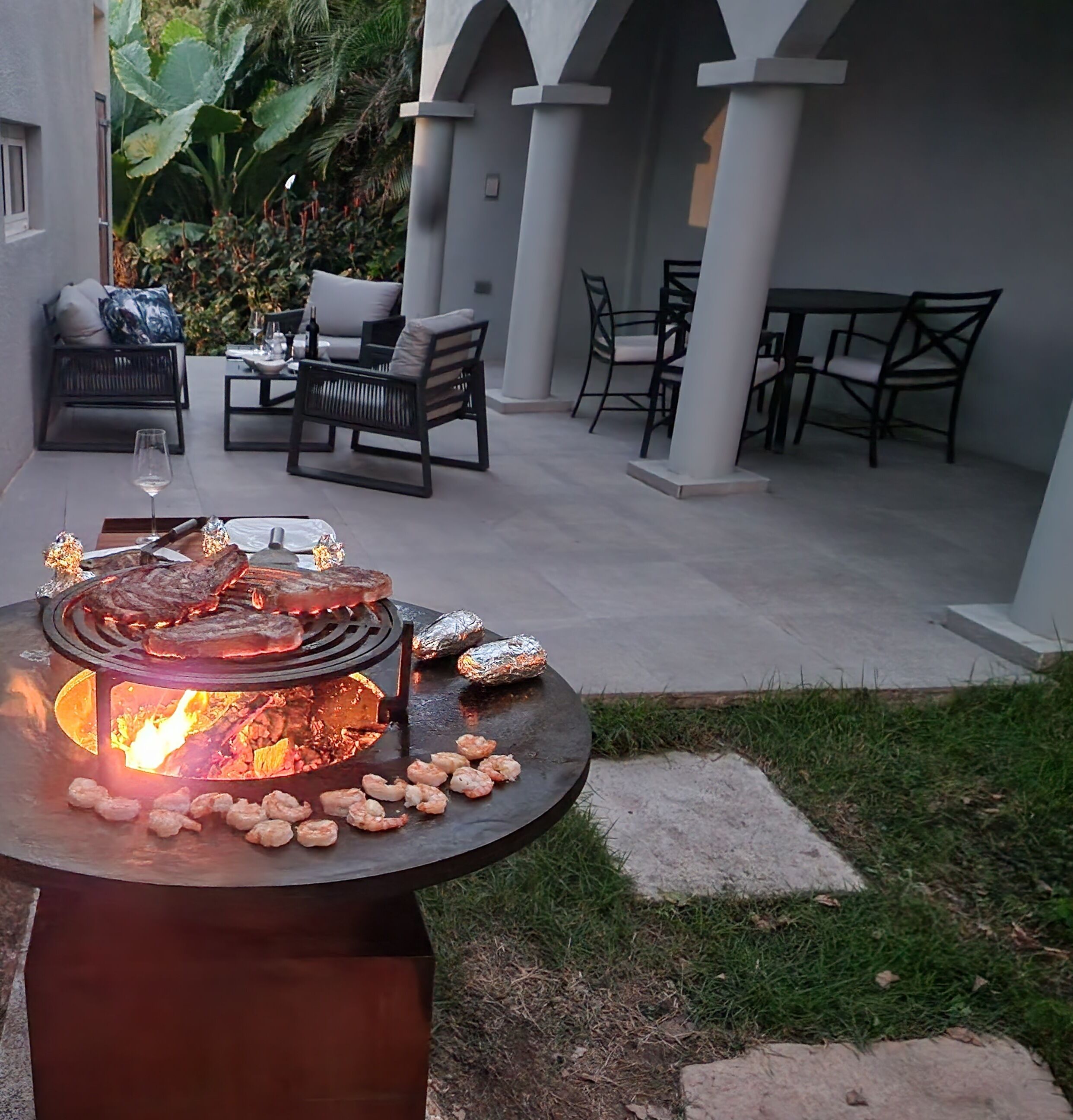 An outdoor patio with a grill, seating area, and a view of the surrounding garden.