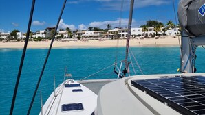 Cubierta de un velero con vista a una playa y edificios al fondo.