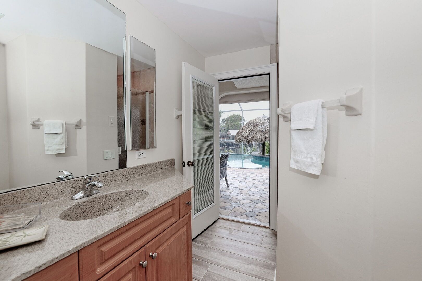 A modern bathroom with a granite countertop, a large mirror, and a door leading to a pool area.