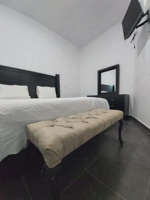 A bedroom with a bed, a bench, a dresser, and a TV mounted on the wall. - Hotel Casa Vega (Ezequiel Montes)