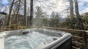 Un jacuzzi rodeado de árboles y una terraza de madera, bajo un cielo despejado.
