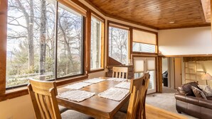 Una habitación amplia con una mesa de comedor de madera, ventanas grandes, un sofá de cuero marrón y una escalera que sube a un nivel superior.