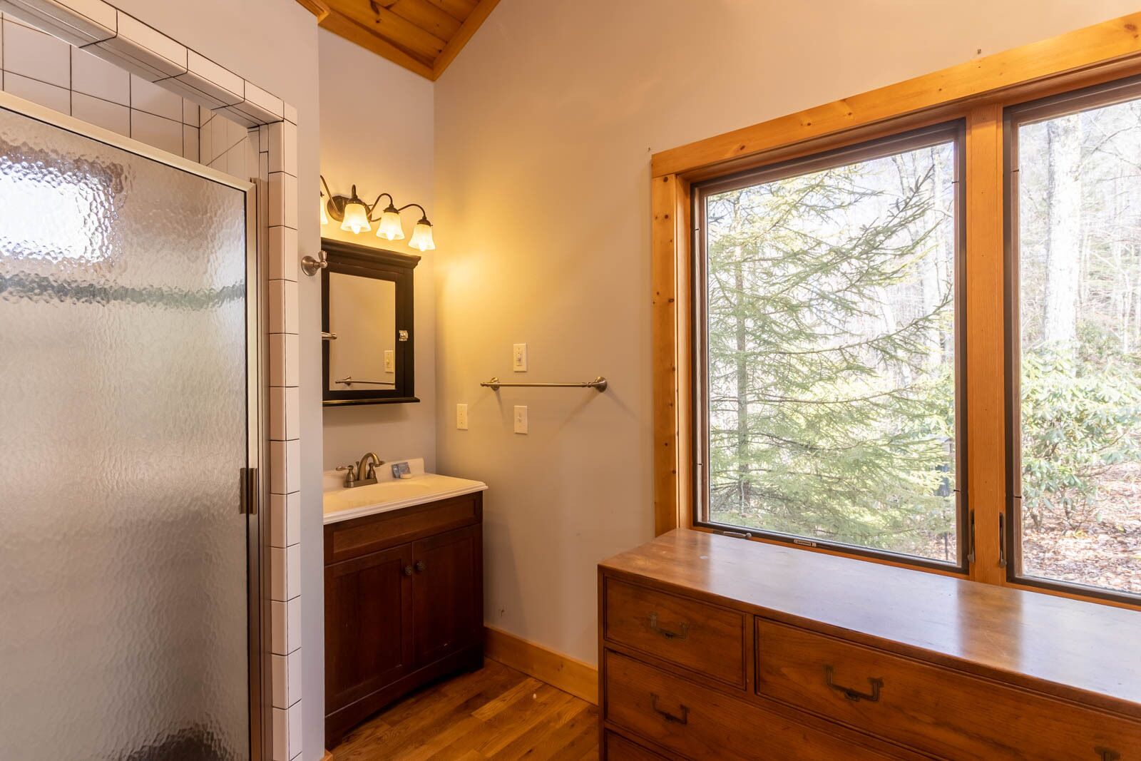 A bathroom with a wooden vanity, a mirror, a sink, and a window with a view of trees.