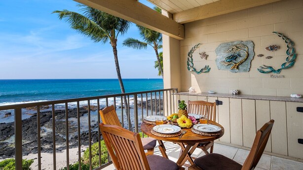 A balcony with a table set for two, overlooking a rocky beach and the ocean. - 🏖️Direct Ocean Front | Close to Town | AC | Upper Floor (Kailua Kona)