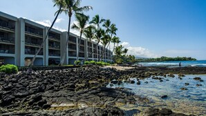 A hotel with multiple floors, a rocky shoreline, and palm trees. - 🏖️Direct Ocean Front | Close to Town | AC | Upper Floor (Kailua Kona)