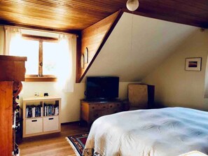 A bedroom with a bed, a wooden cabinet, a television, and a window with curtains.