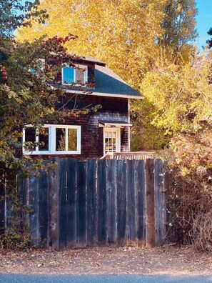 A two-story house with a dark exterior, white-framed windows, and a wooden fence in front.