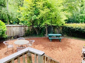 A backyard with a wooden deck, a round table with chairs, a picnic table, and a wooden fence. - Beat the Heat in our Sunny Classic Inverness Home (Inverness)