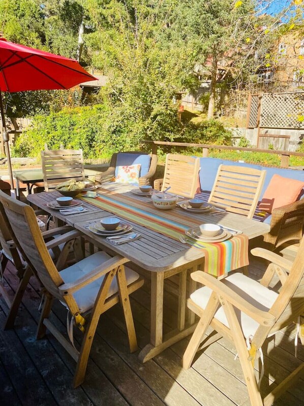 An outdoor wooden dining table with chairs, a red umbrella, and a bench.