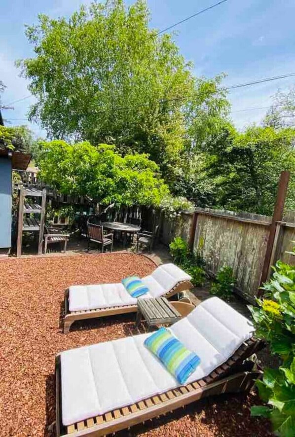 A backyard with two sun loungers, a wooden table, and chairs.