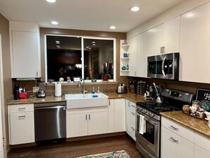 A modern kitchen with white cabinets, stainless steel appliances, a granite countertop, and a large window.