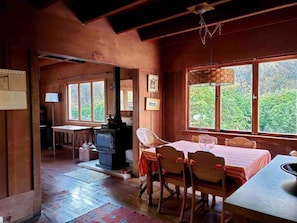 A rustic wooden interior with a dining area, a fireplace, and large windows offering a view of greenery. - Beat the Heat in our Sunny Classic Inverness Home (Inverness)