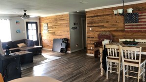 A spacious living room with a wooden floor, a dining area with a table and chairs, and a ceiling fan. - Lake front home in quiet neighborhood & mins away from boat launch and amenities (Many)
