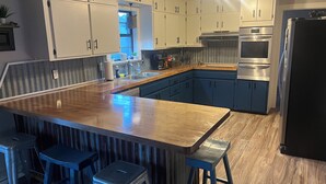 A kitchen with white cabinets, a wooden island with stools, stainless steel appliances, and a window. - Lake front home in quiet neighborhood & mins away from boat launch and amenities (Many)