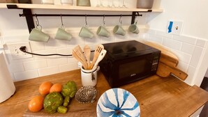 A kitchen with a microwave, a wooden cutting board with vegetables, and a set of green cups hanging on the wall.