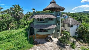 A multi-story building with a thatched roof, surrounded by lush greenery and palm trees.