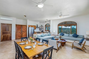 A spacious living area with a dining table set for four, a sofa, and a kitchen in the background.