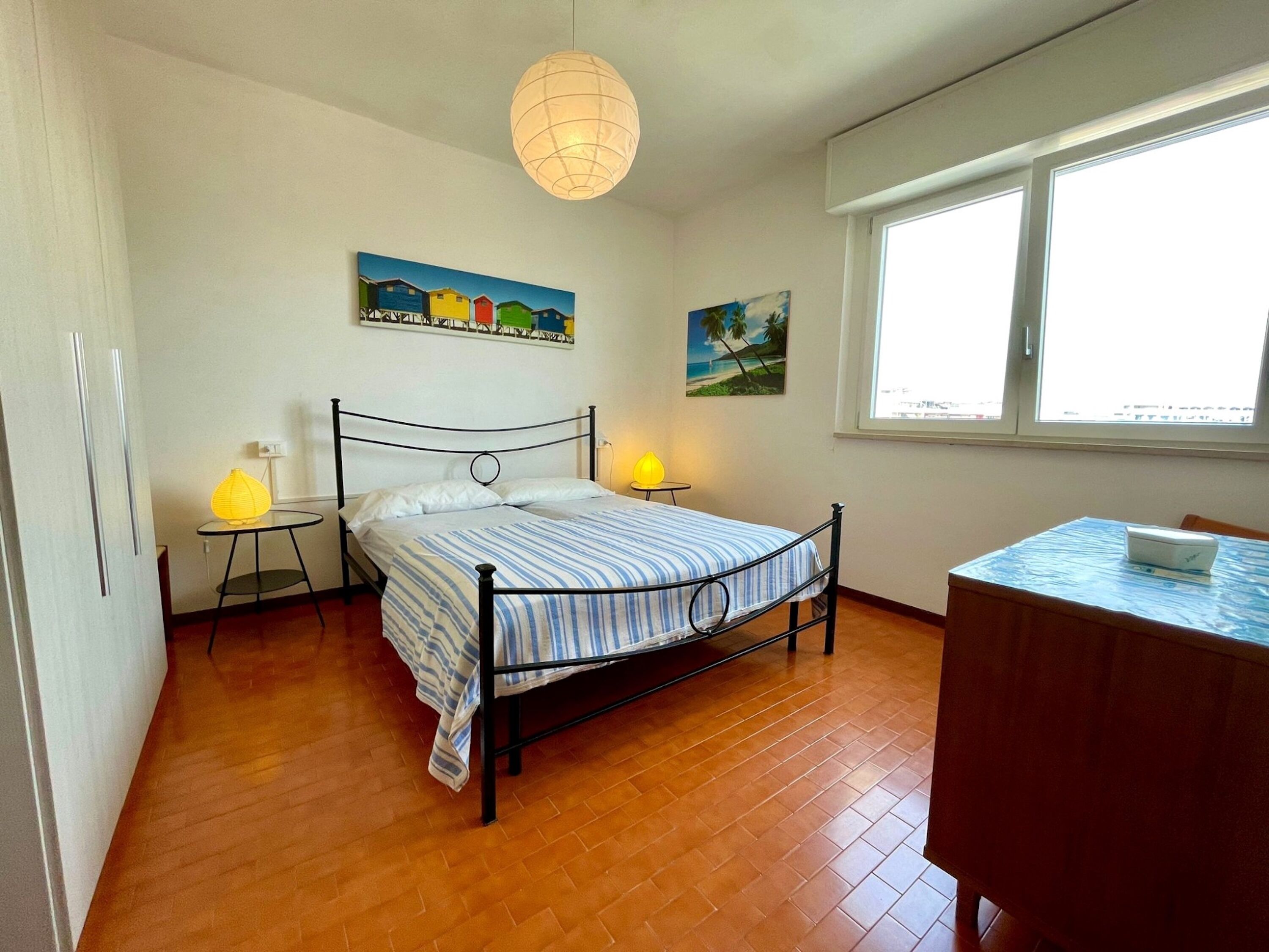 Un dormitorio con cama, lámparas de noche, un escritorio y una ventana.