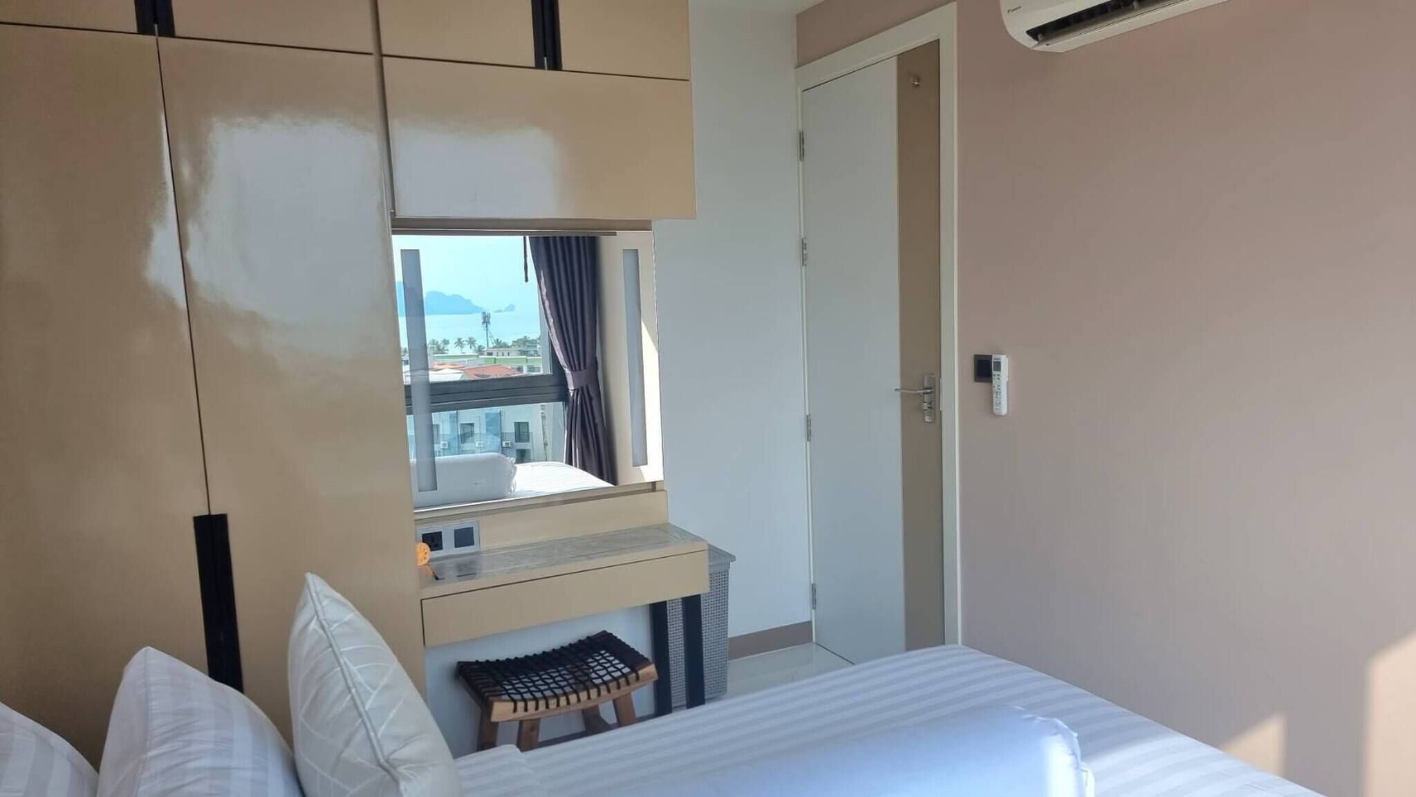 A hotel room with a bed, a small bench, a window with curtains, a wardrobe, and a door.