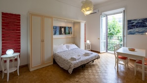 A bedroom with a bed, a wardrobe, a dining table, and a balcony with a view.
