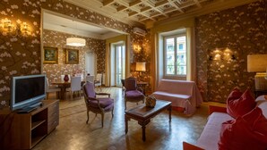 A room with a wooden floor, a television, a sofa, and a dining area with chairs and a table.