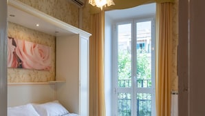 A hotel room with a bed, a chair, a large window, and a painting on the wall.