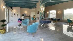 A spacious room with a high ceiling, a marble floor, and a view of the city. There are several seating areas with modern chairs and a round table. - Room in B&B - Relais Dea Degli Ulivi House (Agrigento)