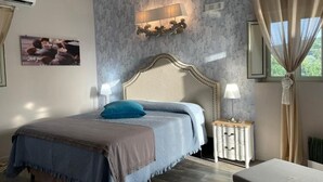 A bedroom with a large bed, a nightstand, a wall-mounted lamp, and a window with curtains. - Room in B&B - Relais Dea Degli Ulivi House (Agrigento)