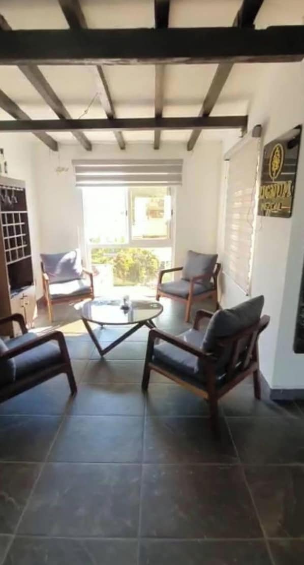 A room with a tiled floor, two wooden chairs with cushions, a small table, and a window with blinds.