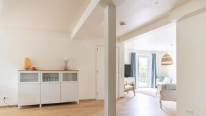 A spacious living area with a wooden floor, a white cabinet with glass doors, and a view of a balcony with a sofa and curtains. - Group Apartment on Ameland by De Vleijen (Nes)