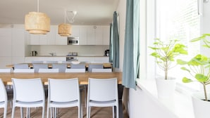 A modern kitchen with white cabinets, a wooden dining table, and two hanging wicker chandeliers. - Group Apartment on Ameland by De Vleijen (Nes)