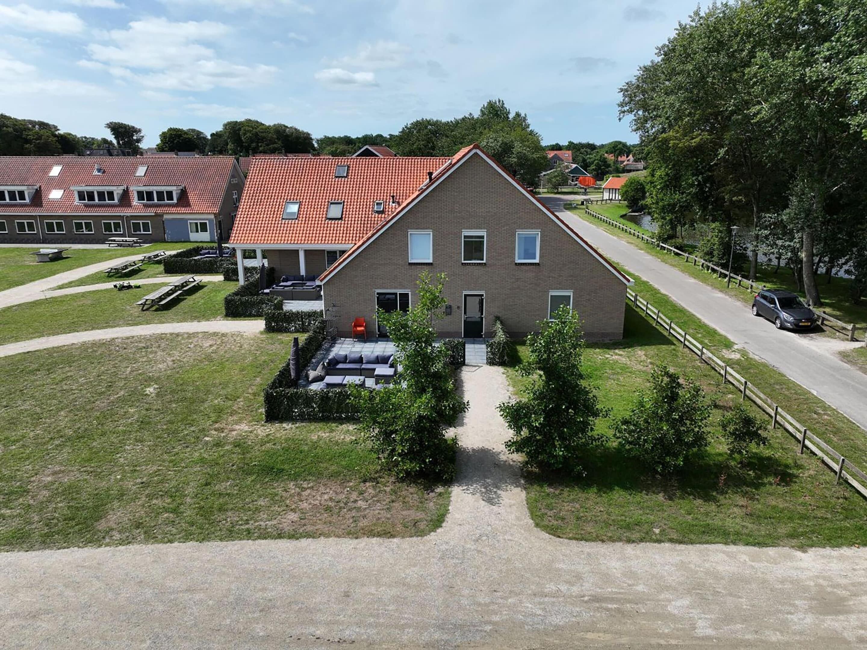 Un edificio a due piani con tetto in tegole rosse, vialetto lastricato e piccolo giardino con panchine e sentiero.