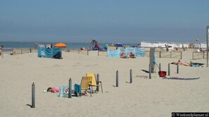 A beach with tents, beach chairs, and a lifeguard stand. - Group Apartment on Ameland by De Vleijen (Nes)