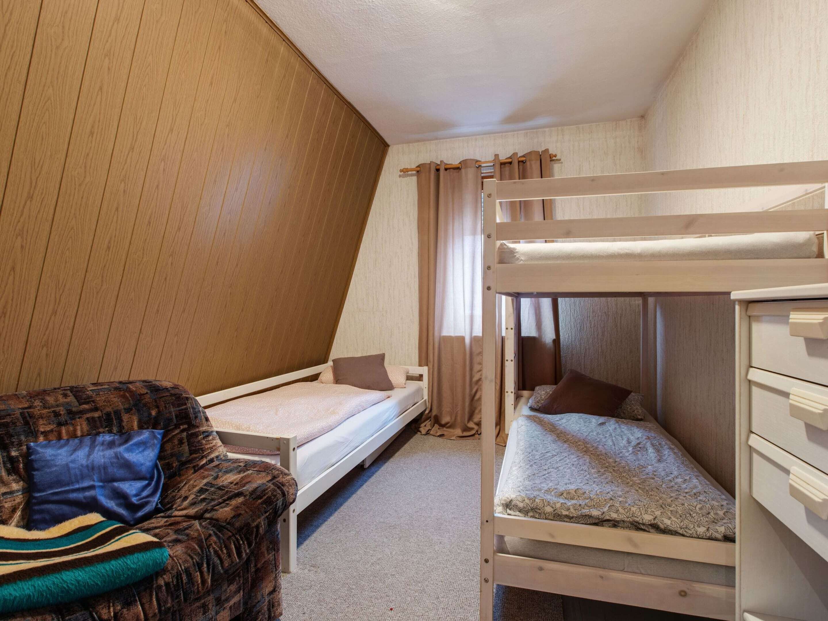 A dorm-style room with bunk beds, a single bed, a wooden wardrobe, and a patterned sofa.