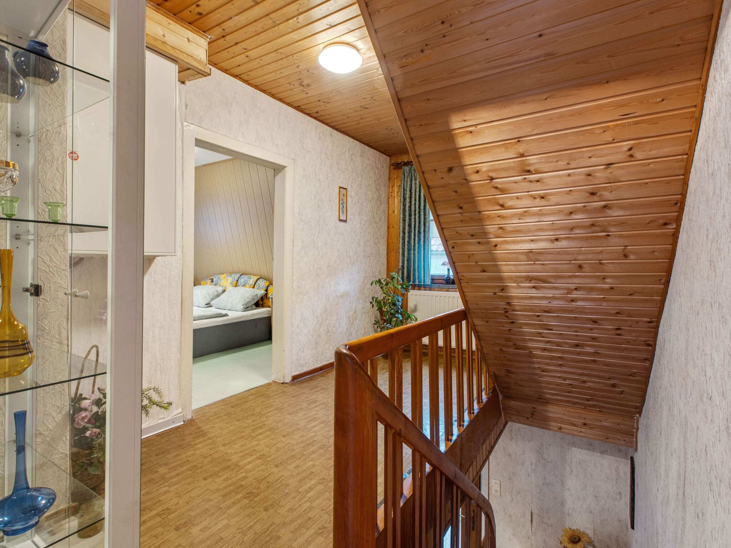 A wooden staircase leading to a bedroom with a bed and a window.