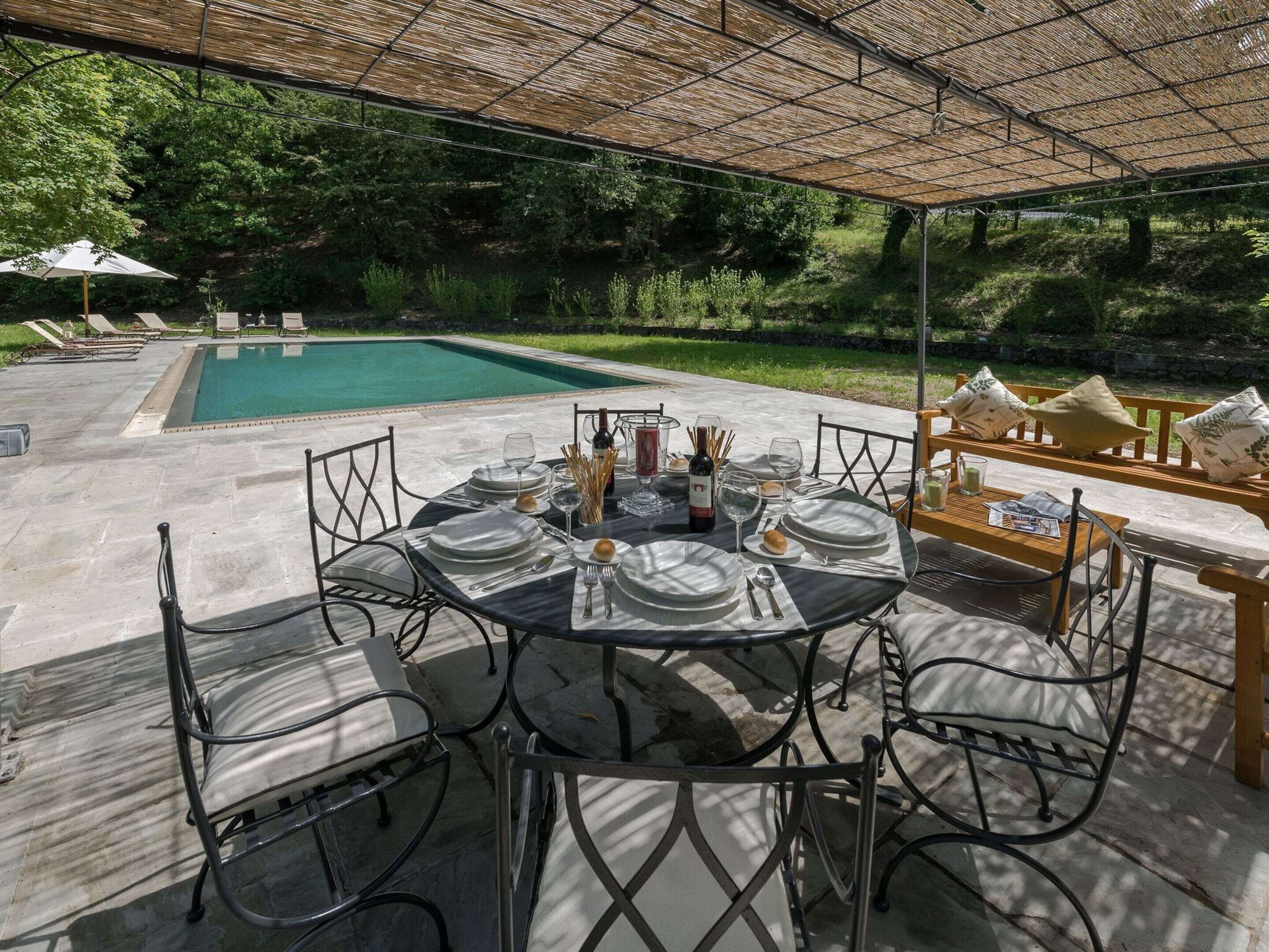 An outdoor dining area with a pool, surrounded by greenery.