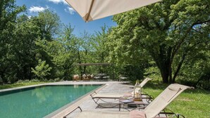 A poolside area with lounge chairs and a table, surrounded by trees. - Belvilla by OYO Villa Arnia (Reggello)